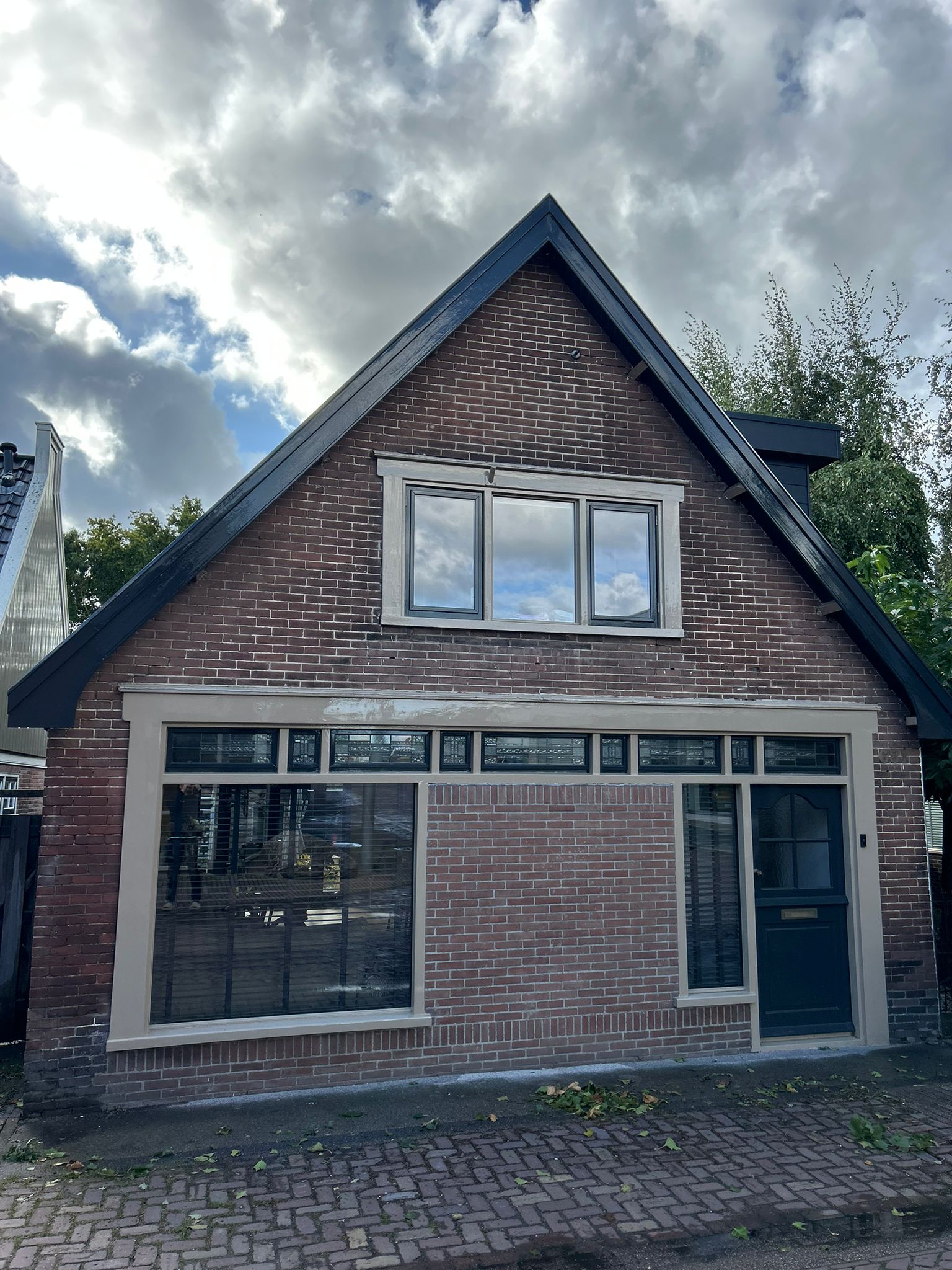 Bakstenen voorgevel met antracietgrijs geschilderde daklijsten, crèmekleurige kozijnen en een donkerblauwe voordeur